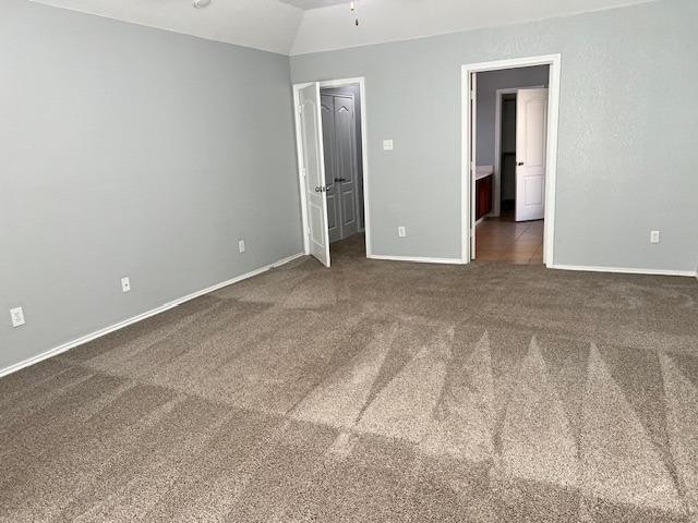 unfurnished bedroom featuring a walk in closet, dark carpet, vaulted ceiling, and ensuite bathroom