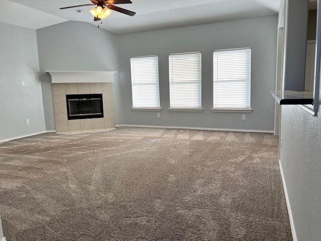 unfurnished living room featuring a tiled fireplace, lofted ceiling, light carpet, and ceiling fan