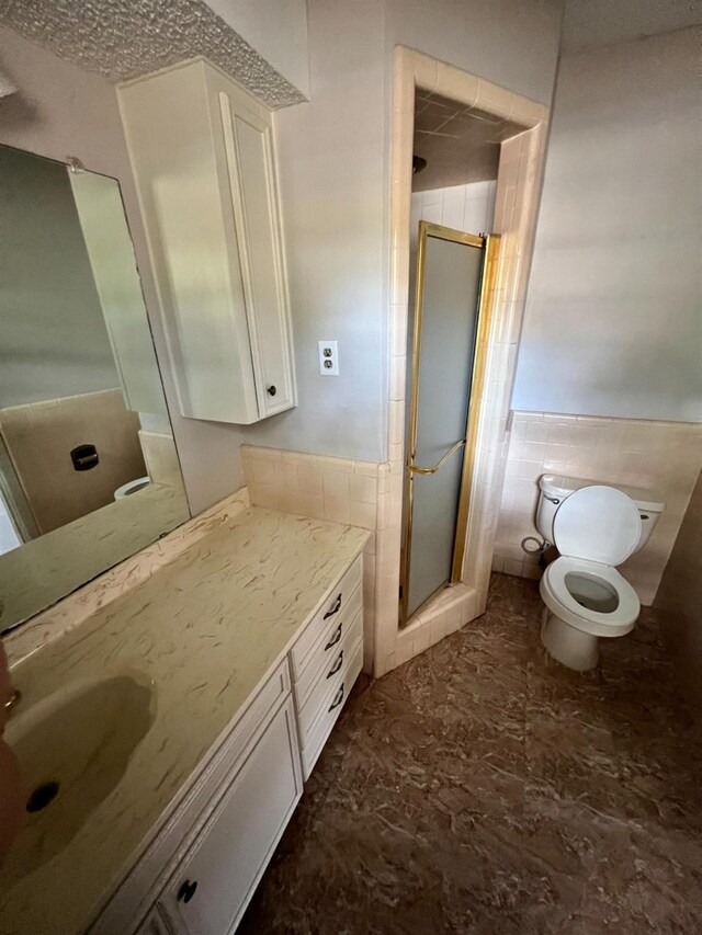 bathroom with tile walls, vanity, a shower with shower door, and toilet