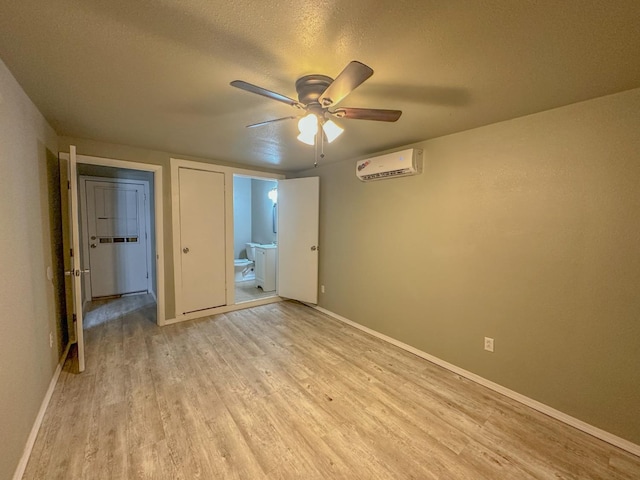 unfurnished bedroom featuring ceiling fan, a wall unit AC, connected bathroom, a textured ceiling, and light wood-type flooring