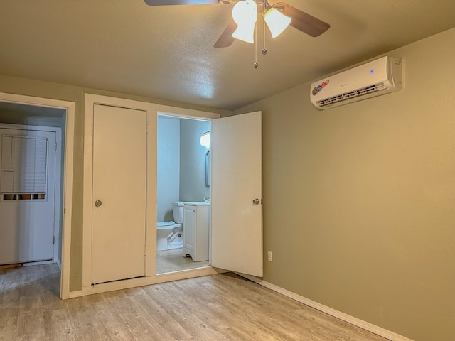 unfurnished bedroom with connected bathroom, sink, a wall unit AC, ceiling fan, and light hardwood / wood-style floors