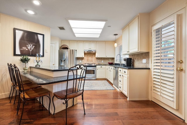 314 York Ave, Lubbock, TX 79416 - kitchen featuring appliances with stainless steel finishes, under cabinet range hood, a peninsula, a breakfast bar area, and backsplash