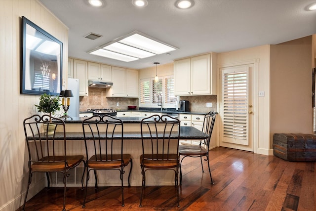 314 York Ave, Lubbock, TX 79416 - kitchen with a peninsula, a kitchen breakfast bar, decorative backsplash, dark wood-style flooring, and recessed lighting