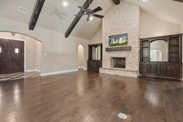 unfurnished living room with ceiling fan, high vaulted ceiling, dark hardwood / wood-style floors, a stone fireplace, and beamed ceiling