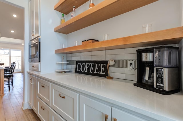 kitchen with built in microwave, white cabinetry, tasteful backsplash, and light hardwood / wood-style flooring