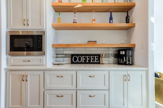 bar with built in microwave, white cabinetry, and decorative backsplash