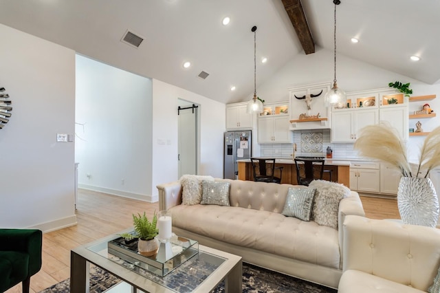 living room with light hardwood / wood-style flooring, high vaulted ceiling, a barn door, and beamed ceiling