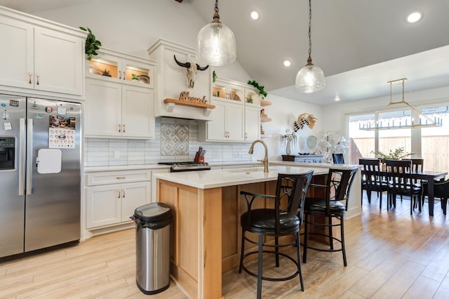 kitchen with appliances with stainless steel finishes, a kitchen island with sink, white cabinets, and decorative light fixtures