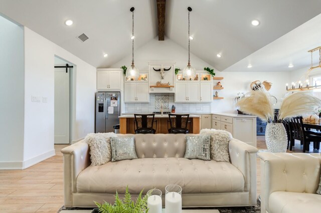 living room featuring a barn door, high vaulted ceiling, beam ceiling, and light wood-type flooring