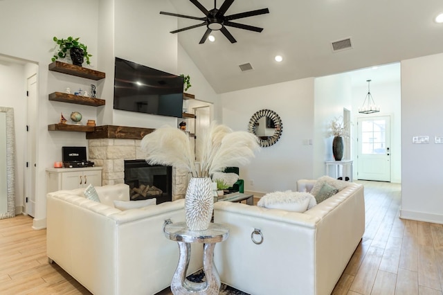 living room featuring high vaulted ceiling, a stone fireplace, ceiling fan with notable chandelier, and light wood-type flooring