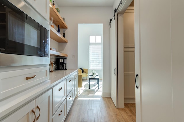 kitchen with built in microwave, white cabinetry, a barn door, and light hardwood / wood-style floors