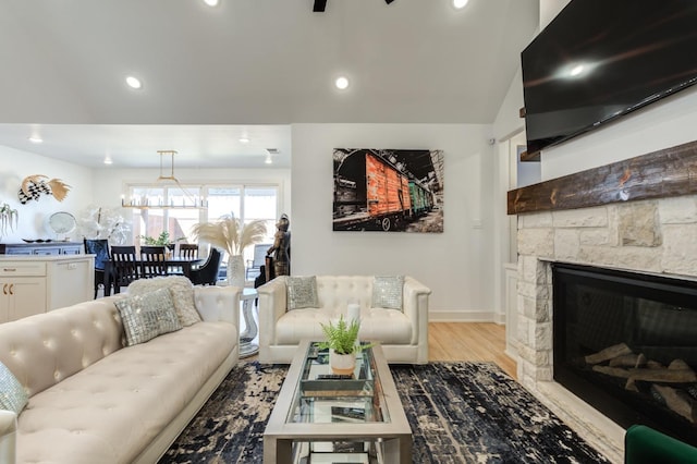 living room featuring lofted ceiling, a stone fireplace, and light hardwood / wood-style floors