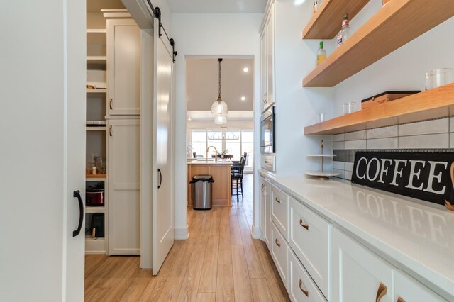 kitchen featuring white cabinetry, hanging light fixtures, light hardwood / wood-style floors, and a barn door