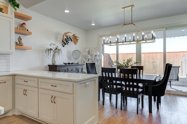 kitchen with tasteful backsplash, light hardwood / wood-style flooring, kitchen peninsula, pendant lighting, and white cabinets