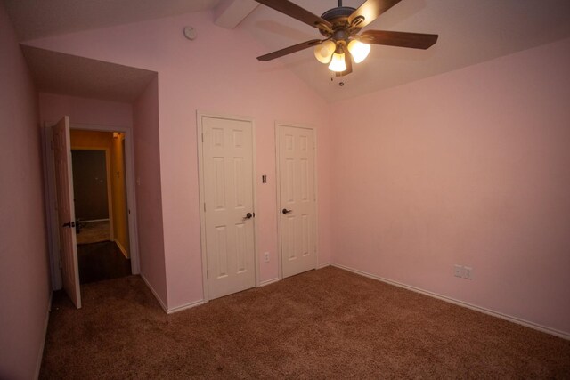 unfurnished bedroom with dark carpet, ceiling fan, and lofted ceiling with beams