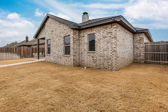 rear view of property featuring a yard, brick siding, a fenced backyard, and a patio area
