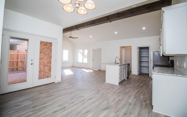 kitchen featuring lofted ceiling with beams, white cabinets, decorative backsplash, a center island with sink, and french doors