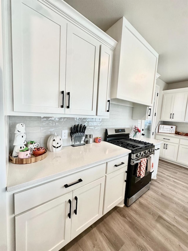 kitchen with gas stove, white cabinets, light hardwood / wood-style floors, and decorative backsplash