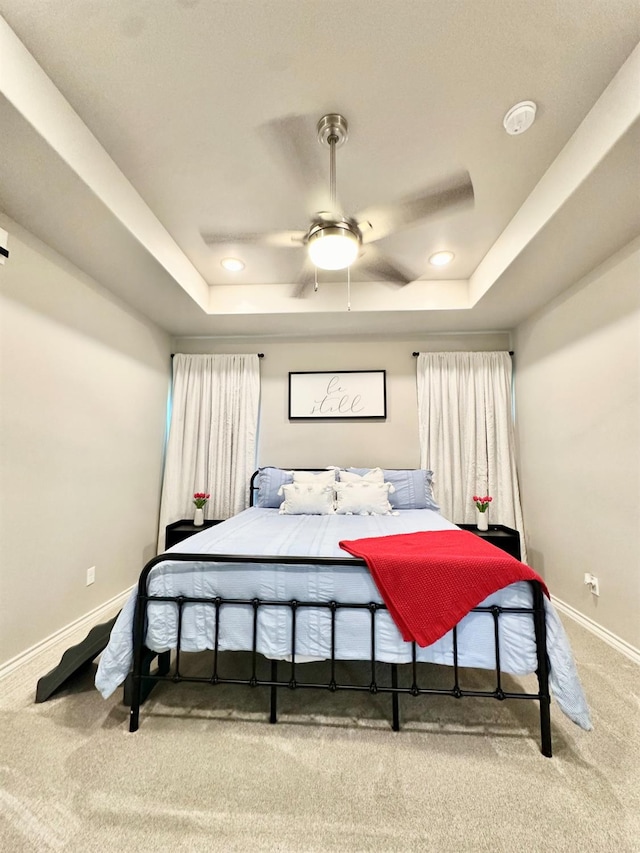 carpeted bedroom with ceiling fan and a tray ceiling