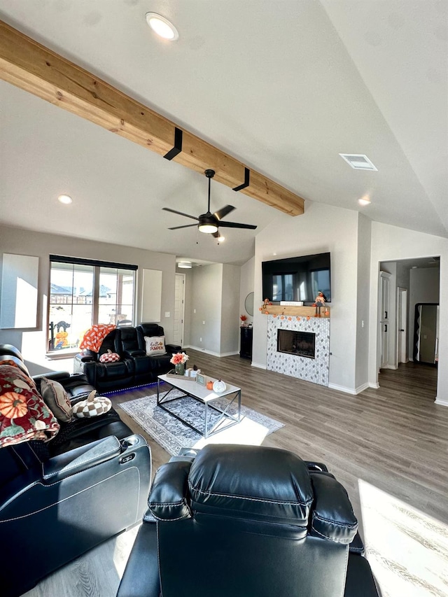 living room featuring a tiled fireplace, hardwood / wood-style floors, lofted ceiling with beams, and ceiling fan