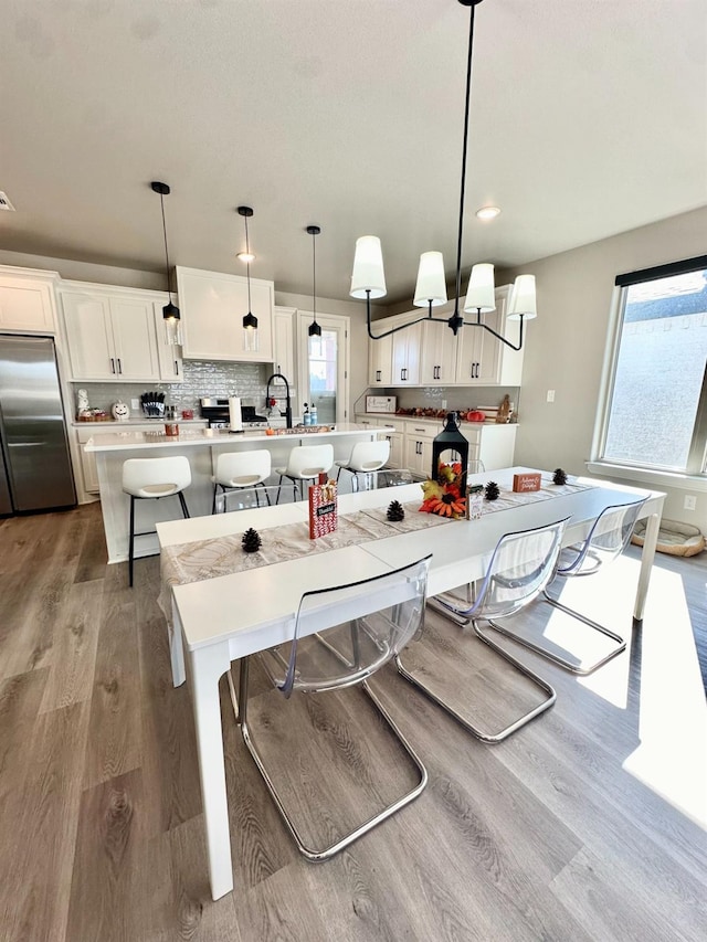 kitchen with a breakfast bar, hanging light fixtures, white cabinets, a center island with sink, and stainless steel built in fridge