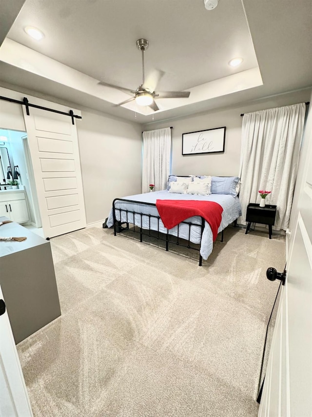 carpeted bedroom featuring a barn door, ceiling fan, and a tray ceiling