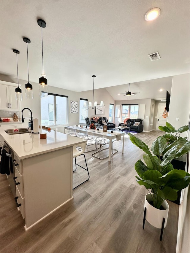 kitchen with white cabinetry, hanging light fixtures, light hardwood / wood-style flooring, and an island with sink