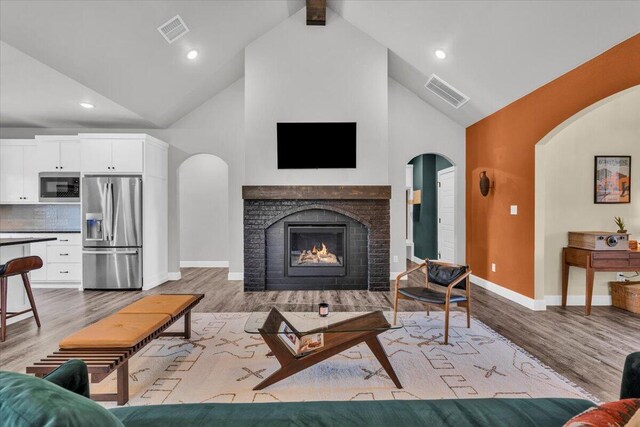6803 52nd St, Lubbock, TX 79407 - living room featuring arched walkways, light wood-style flooring, baseboards, high vaulted ceiling, and a fireplace