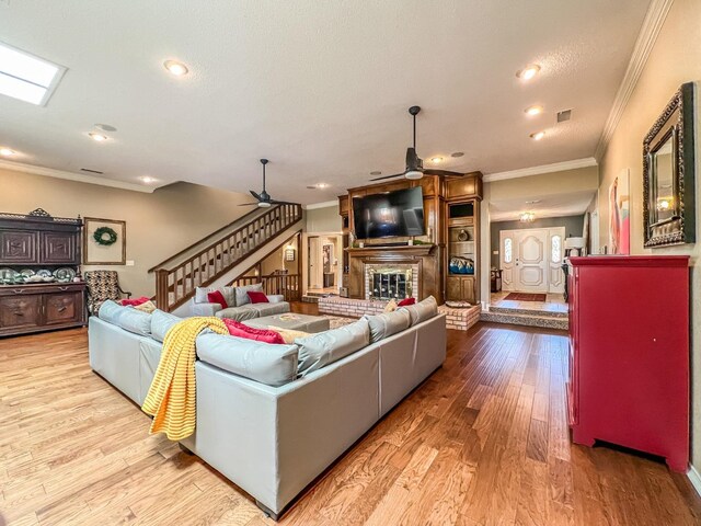 living room with light hardwood / wood-style flooring, a textured ceiling, ornamental molding, ceiling fan, and a fireplace