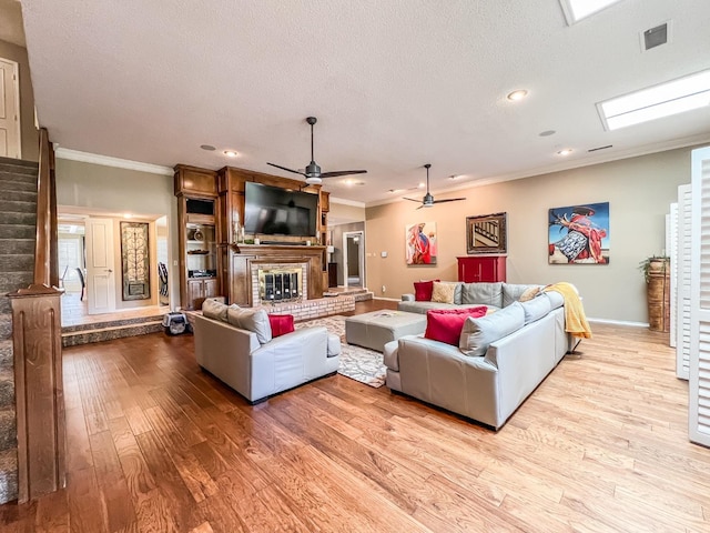 living room with crown molding, ceiling fan, light hardwood / wood-style floors, a textured ceiling, and a brick fireplace