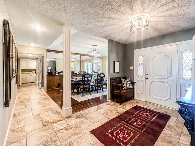 entrance foyer featuring ornate columns, a textured ceiling, and an inviting chandelier