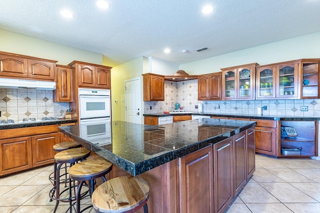 4306 Alcove Ave, Lubbock, TX 79407 - kitchen with a textured ceiling, under cabinet range hood, a breakfast bar, a kitchen island, and backsplash