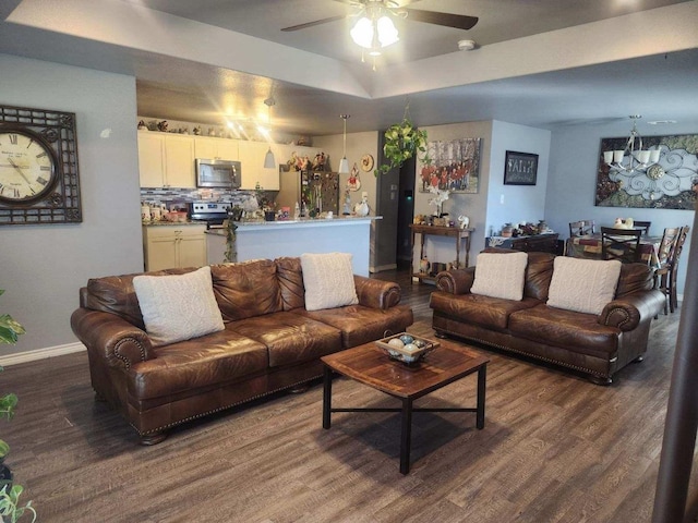 living room with dark wood-type flooring, ceiling fan with notable chandelier, and a tray ceiling