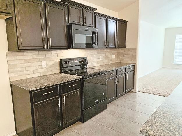 kitchen with dark brown cabinetry, stone countertops, light tile patterned floors, decorative backsplash, and black appliances