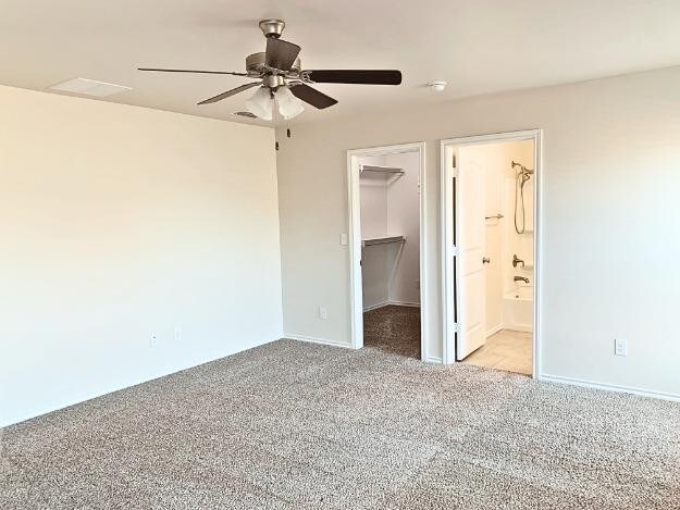 unfurnished bedroom with ensuite bathroom, a spacious closet, light carpet, a closet, and ceiling fan