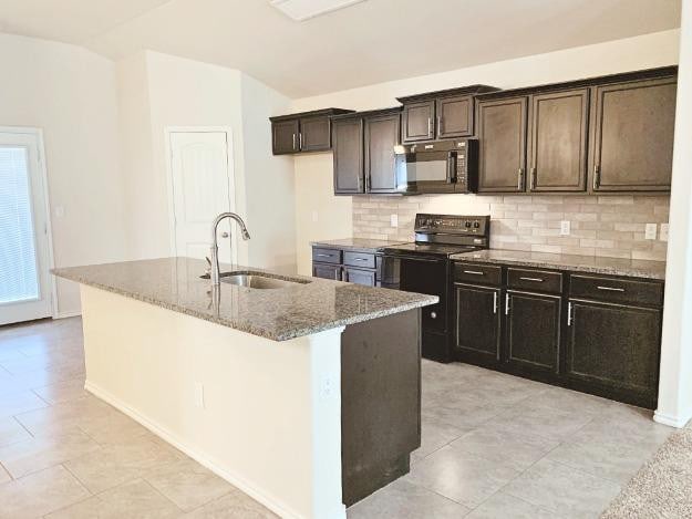 kitchen with sink, a kitchen island with sink, black appliances, vaulted ceiling, and dark stone counters