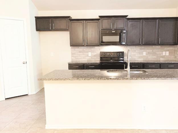 kitchen featuring sink, stove, light stone counters, tasteful backsplash, and dark brown cabinetry