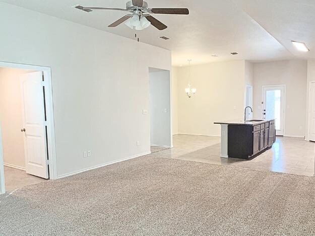 unfurnished living room featuring ceiling fan with notable chandelier, sink, and light colored carpet