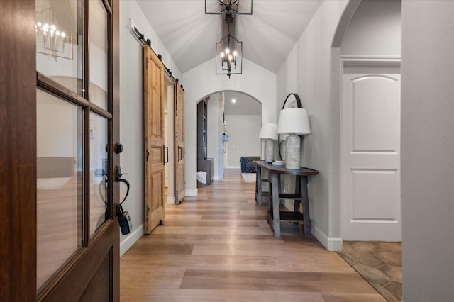 hall with an inviting chandelier, lofted ceiling, a barn door, and light hardwood / wood-style flooring