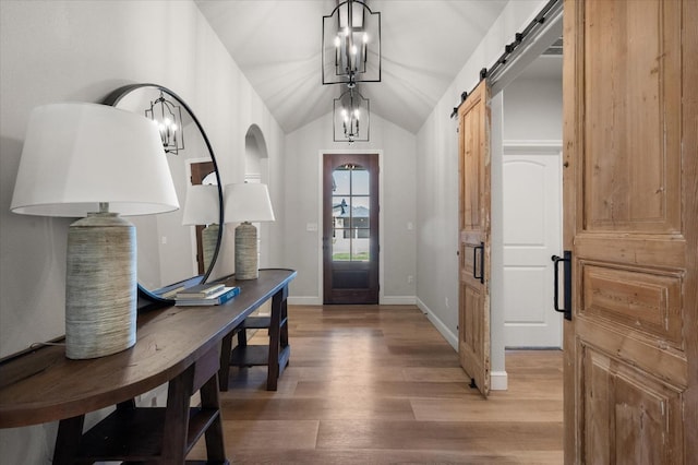 entrance foyer with lofted ceiling, wood-type flooring, a barn door, and a chandelier