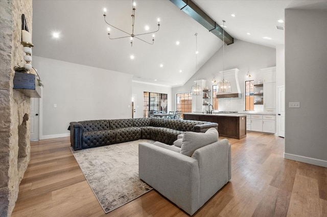 living room featuring sink, high vaulted ceiling, a notable chandelier, light hardwood / wood-style floors, and beamed ceiling