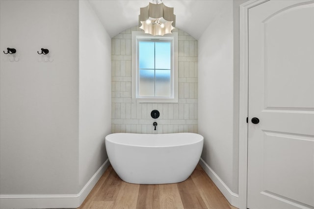 bathroom featuring hardwood / wood-style flooring, a tub, lofted ceiling, and a chandelier