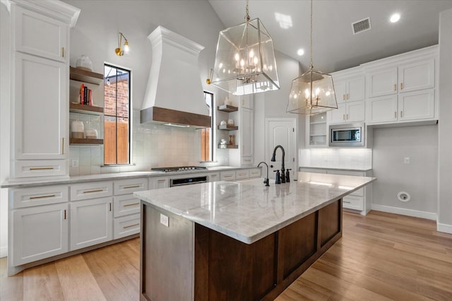 kitchen with white cabinetry, an island with sink, pendant lighting, and stainless steel microwave