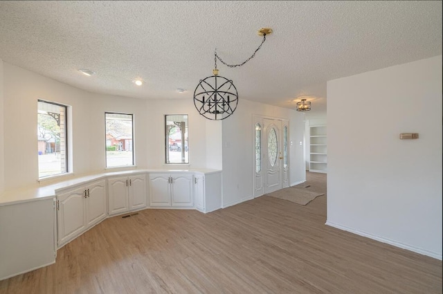 unfurnished dining area with baseboards, a textured ceiling, visible vents, and light wood-type flooring