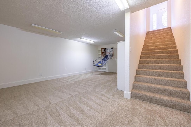 below grade area featuring baseboards, a textured ceiling, carpet flooring, and stairs