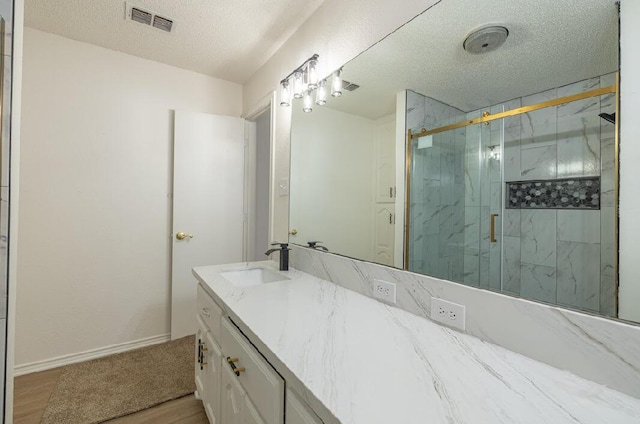 full bathroom featuring a marble finish shower, a textured ceiling, visible vents, wood finished floors, and vanity