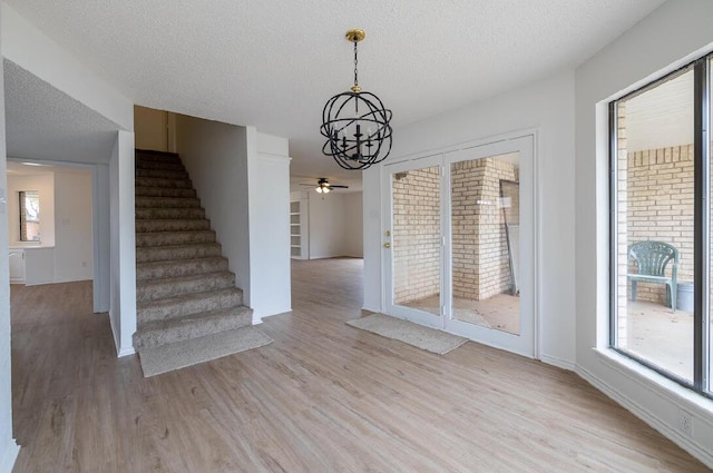 unfurnished dining area with light wood-style flooring, a textured ceiling, baseboards, ceiling fan with notable chandelier, and stairway