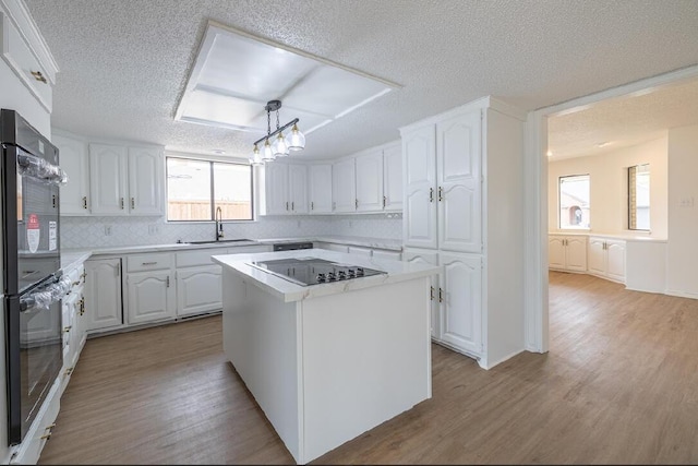 kitchen with light wood-style flooring, a sink, a textured ceiling, white cabinetry, and light countertops