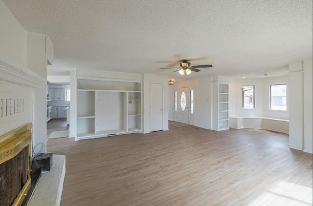 unfurnished living room featuring a ceiling fan, a healthy amount of sunlight, a textured ceiling, and light wood-style flooring