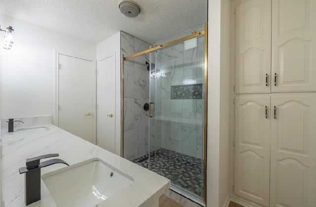 bathroom featuring double vanity, a sink, a marble finish shower, and a textured ceiling